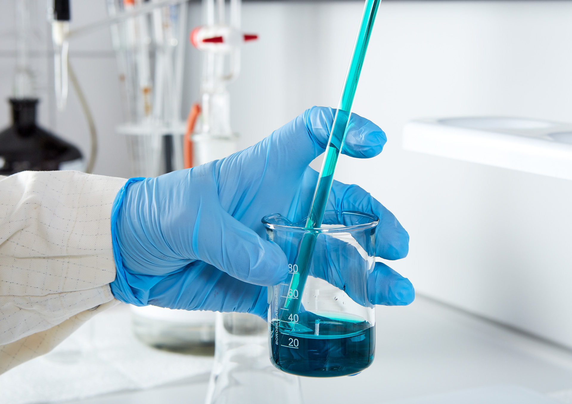 Mitarbeiter im Labor hält ein Glas mit blauer Flüssigkeit