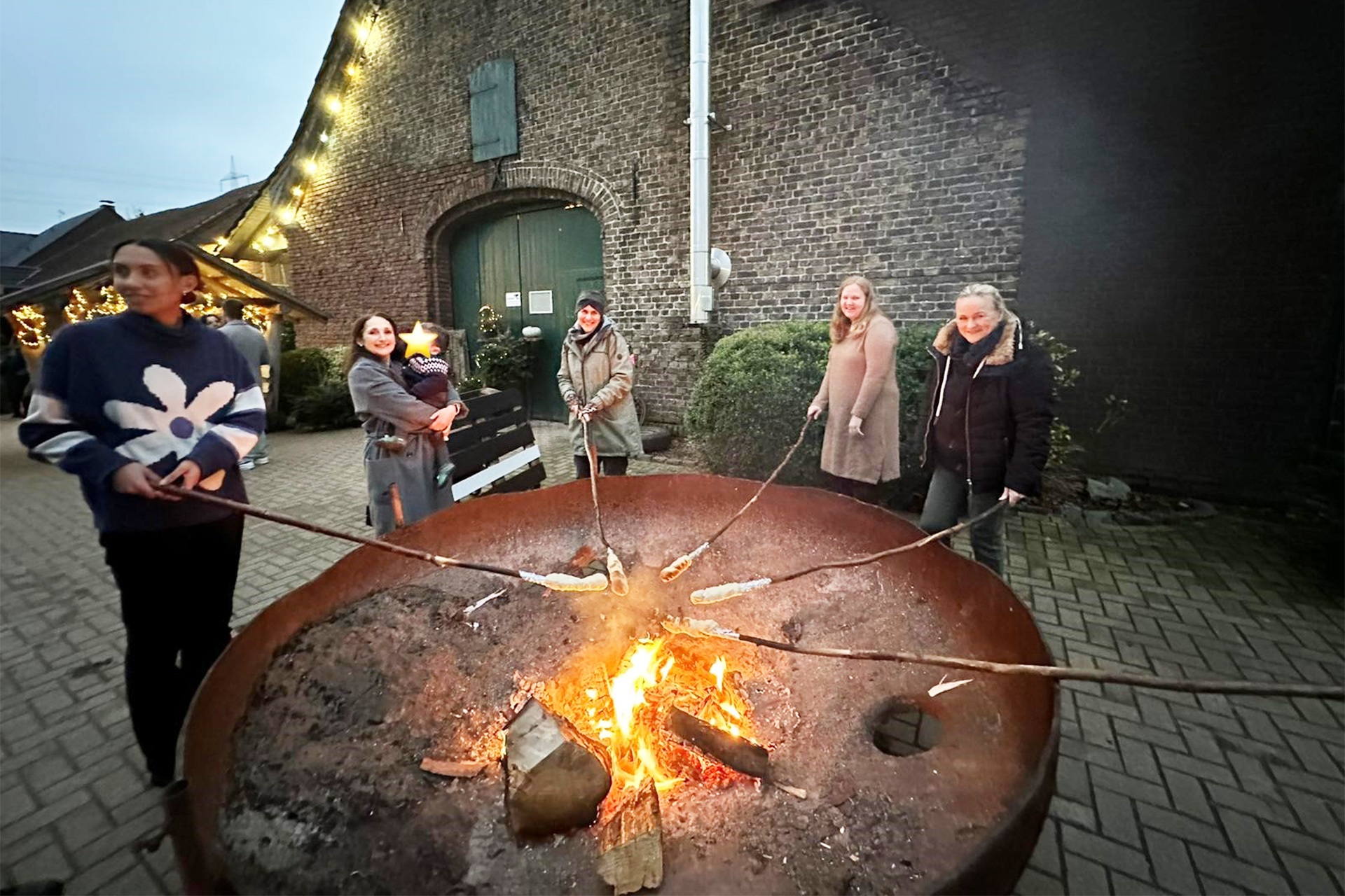 Menschen stehen am Feuer und machen Stockbrot.